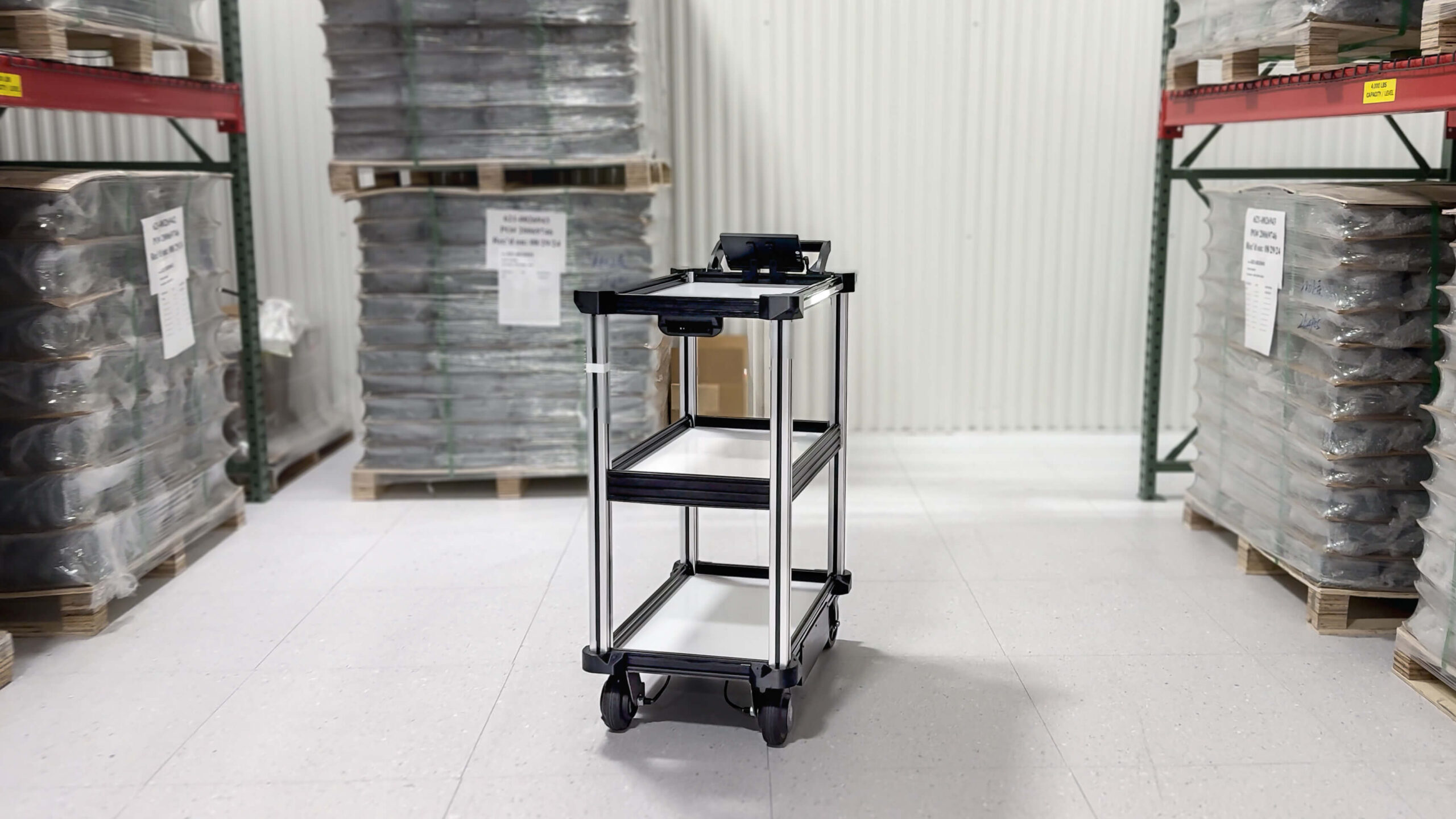 C2 in Manufacturing 4 small Model C2 autonomous delivery cart navigates between warehousing shelves in a busy electronics manufacturing environment while transporting components, supplies, and materials.